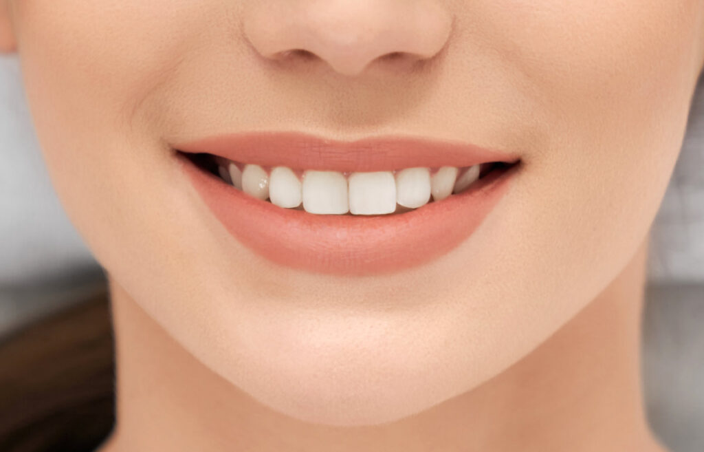 Close up of young attractive woman with beautiful smiling and white teeth on procedure in beautician or dentist. Concept of beauty procedure for skin and for teeth.